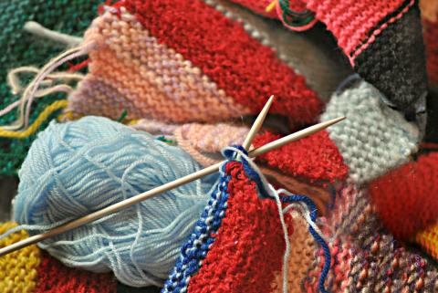 A pile of yarn, partially completing knitting projects, and knitting needles