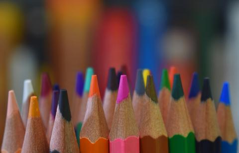 The tips of a few dozen colored pencils in a bundle, with a fuzzy colorful background