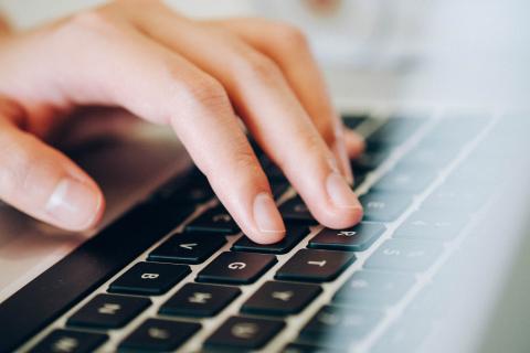 One hand hovering over the keyboard of a laptop