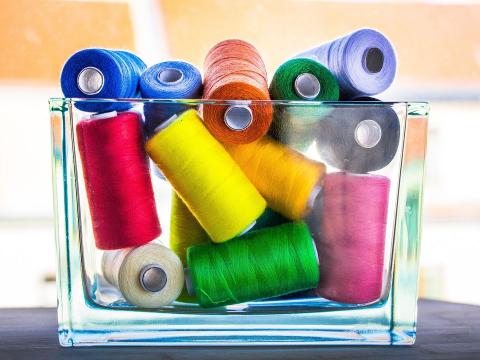 A rectangular glass vase full of several spools of thread in many colors