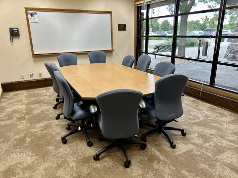 Meeting room with large table in center, surrounded by blue-gray office chairs.