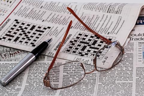 pair of reading glasses and black pen atop newspapers, one of them containing puzzles