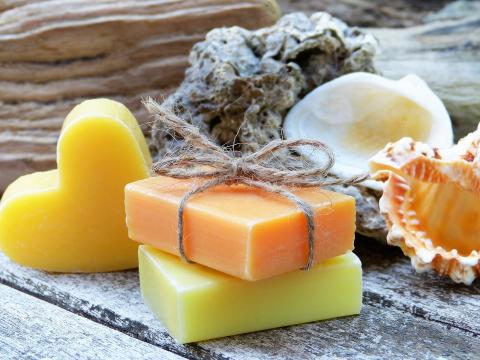 orange and green rectangular bars of soap, one tied with string. yellow heart shaped soap is on its side to the left. sponge and shells are in the background.