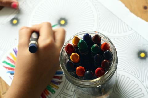 A hand holding a crayon next to a jar of crayons