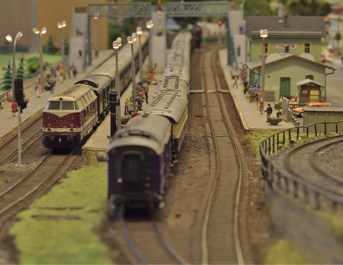 Two toy trains coming down the tracks, through a toy village.