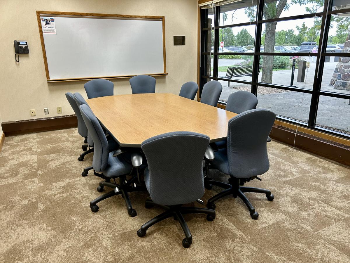 Meeting room with large table in center, surrounded by blue-gray office chairs.