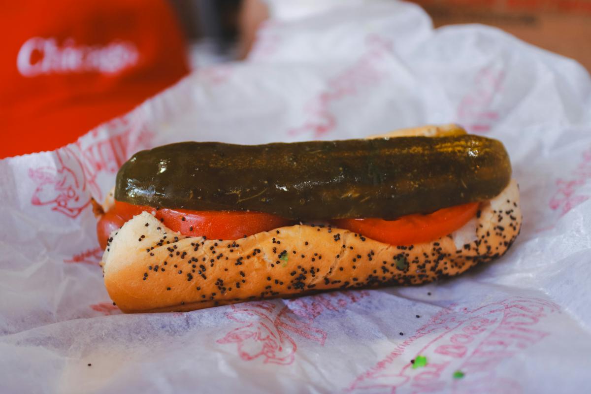 Hot dog on a poppyseed bun with tomato and pickle
